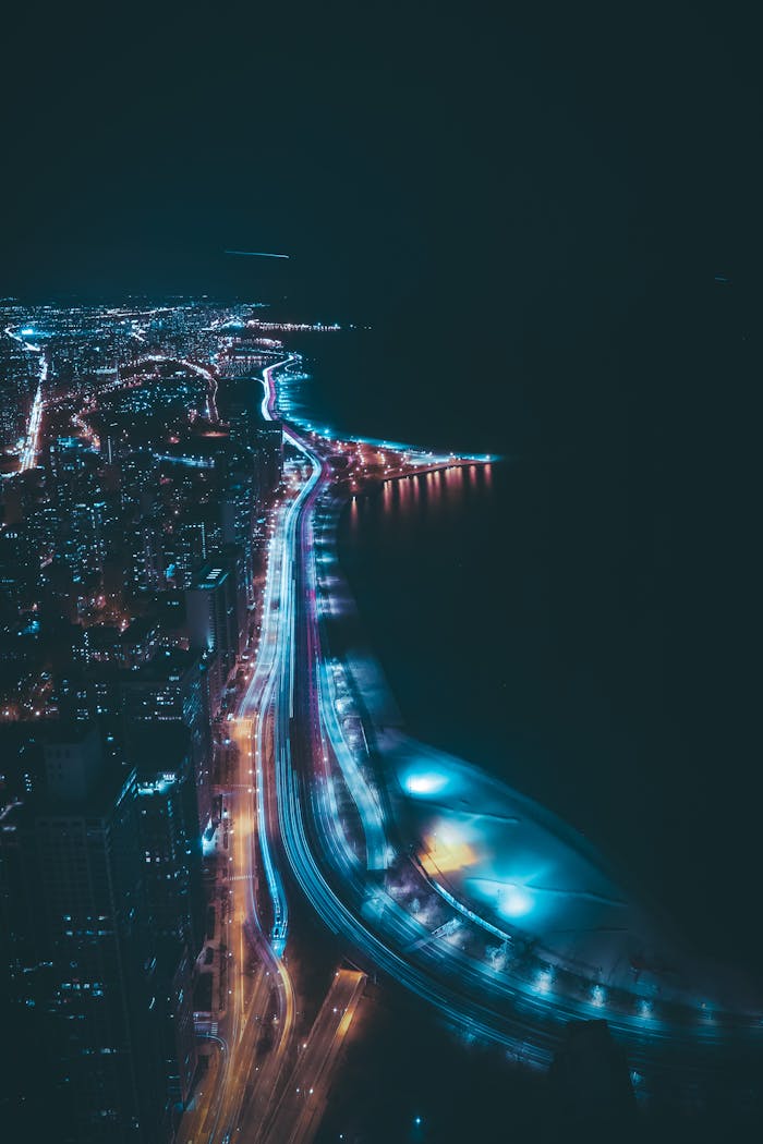 A stunning aerial view of Chicago's skyline at night, featuring dynamic light trails along the highway.